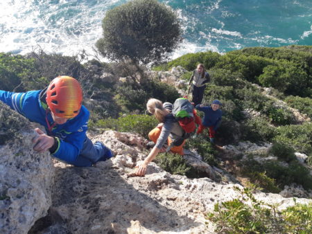 Nils Helsper (RP1, left) managing a short free solo climb on the way back to the car after climbinging in Cala Bota (Mallorca, Spain), Anna Lipp (AU1, right side on the ground) waiting for her turn to climb up with just one arm.